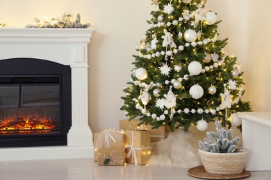 Photo of Decorated Christmas tree with faux fur skirt and gift boxes near fireplace indoors