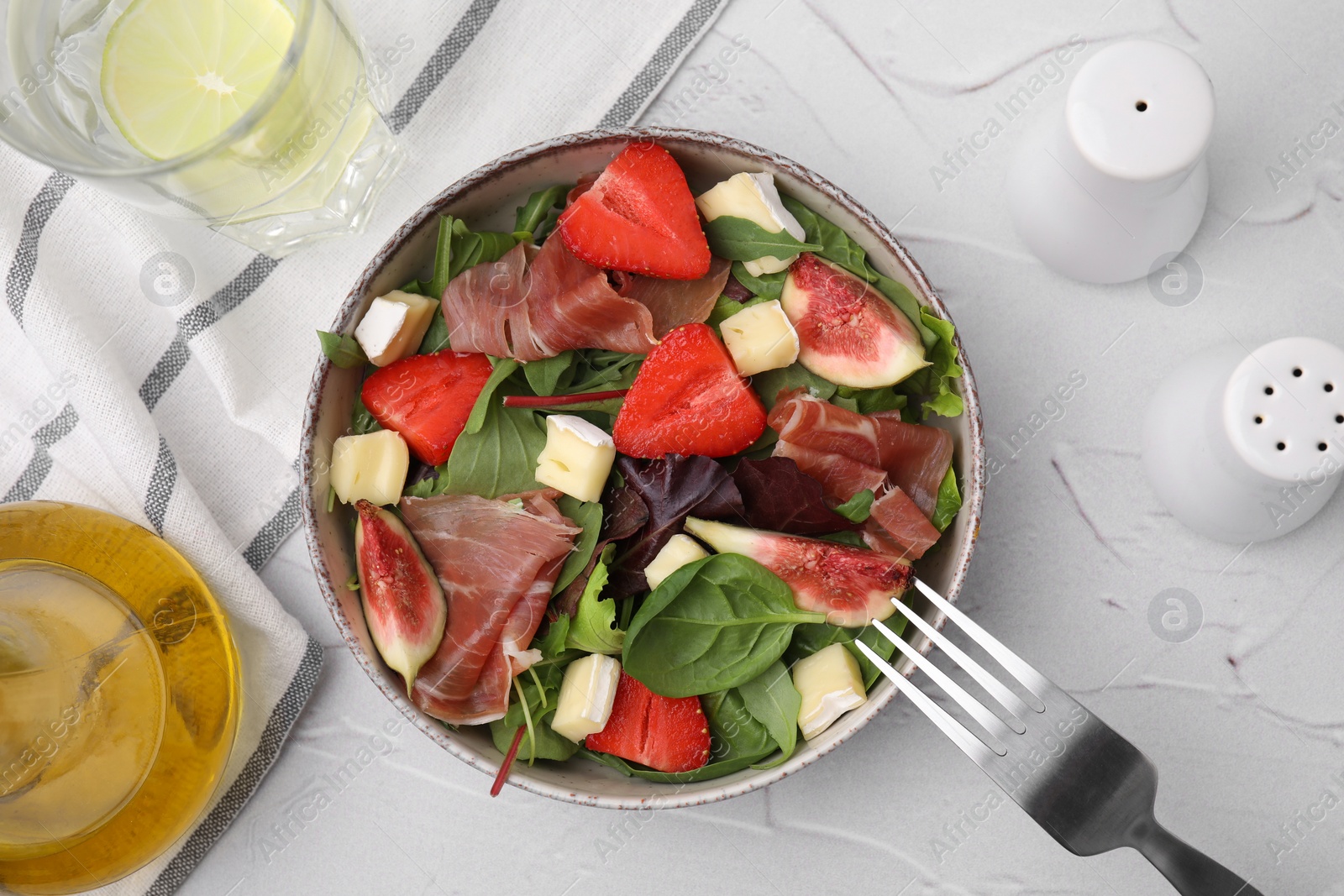 Photo of Tasty salad with brie cheese, prosciutto, strawberries and figs on white textured table, flat lay