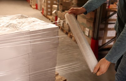 Photo of Worker wrapping boxes in stretch film at warehouse, closeup