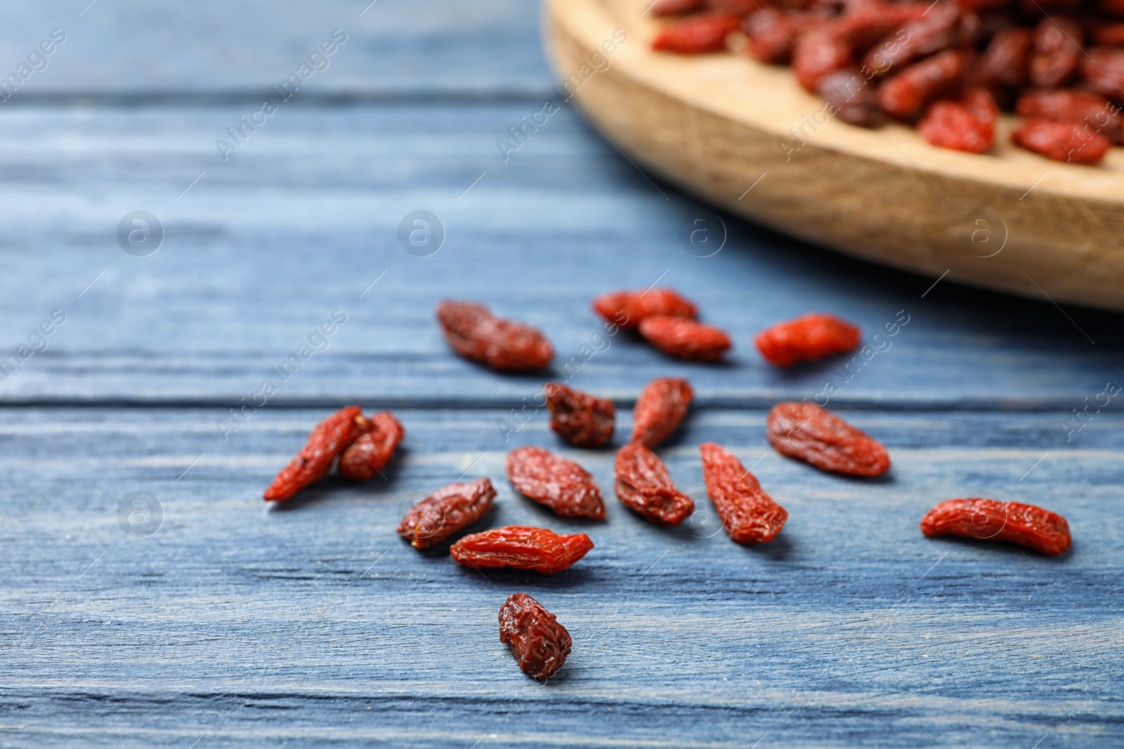 Photo of Dried goji berries on blue wooden table, closeup