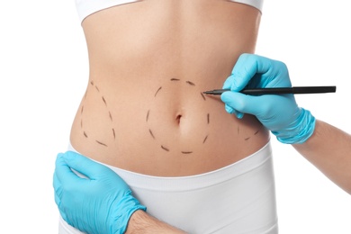 Doctor drawing marks on woman's body for cosmetic surgery operation against white background, closeup