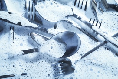 Photo of Different silverware in foam, flat lay. Toned in blue