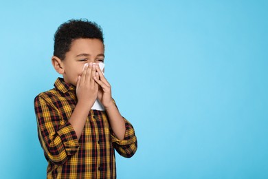 Photo of African-American boy blowing nose in tissue on turquoise background, space for text. Cold symptoms