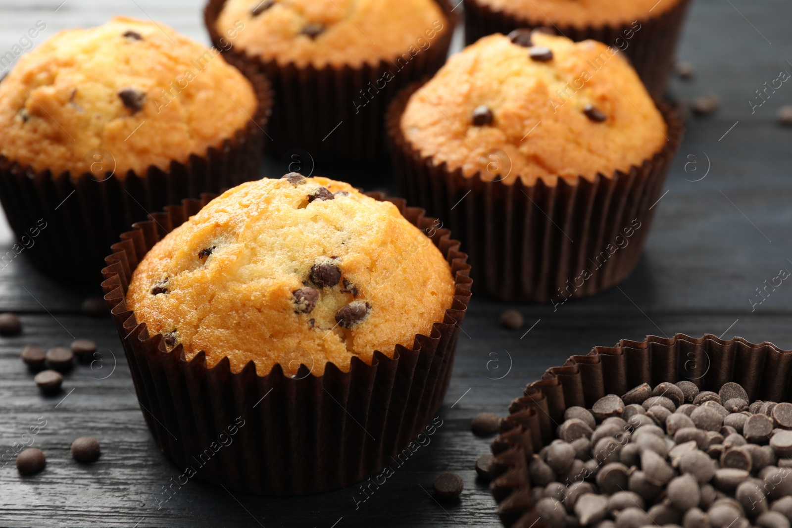 Photo of Delicious freshly baked muffins with chocolate chips on dark gray table, closeup