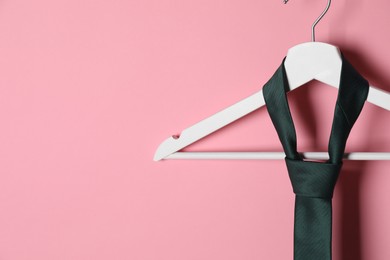 Photo of Hanger with black tie on pink background, closeup. Space for text