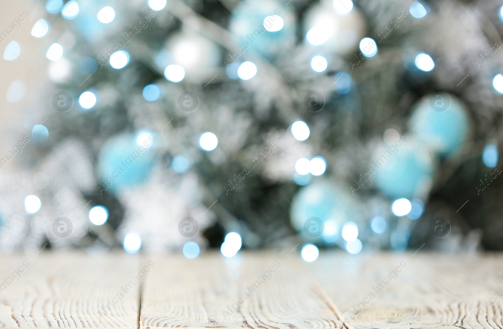 Photo of Empty white wooden table and blurred fir tree with Christmas lights on background, bokeh effect. Space for design