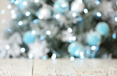 Photo of Empty white wooden table and blurred fir tree with Christmas lights on background, bokeh effect. Space for design