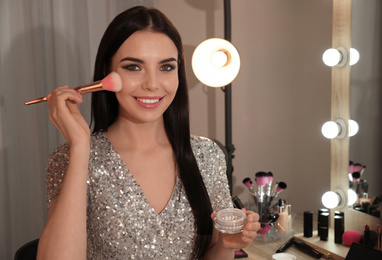 Beautiful young woman applying makeup near mirror in dressing room