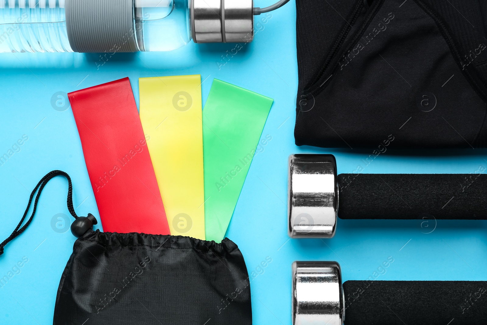 Photo of Flat lay composition with fitness elastic bands and sport accessories on light blue background