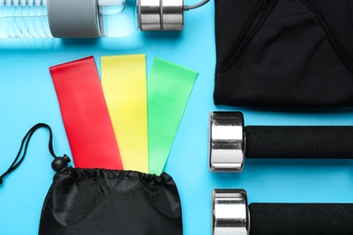 Photo of Flat lay composition with fitness elastic bands and sport accessories on light blue background