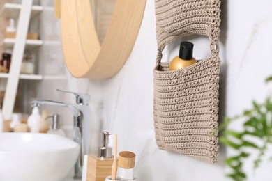 Photo of Storage with cosmetic bottle hanging on white marble wall in bathroom. Stylish accessory