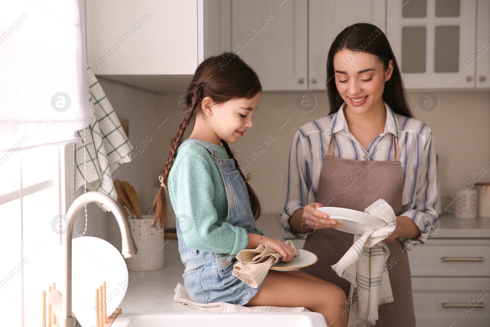 Photo of Mother and daughter wiping dishes together in kitchen