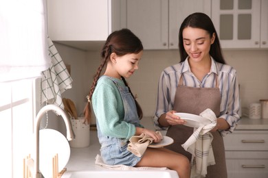 Photo of Mother and daughter wiping dishes together in kitchen