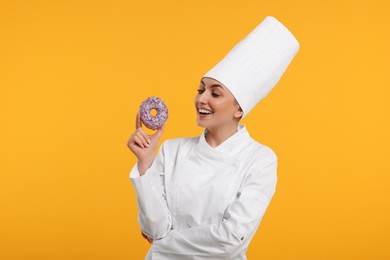 Photo of Happy professional confectioner in uniform holding delicious doughnut on yellow background