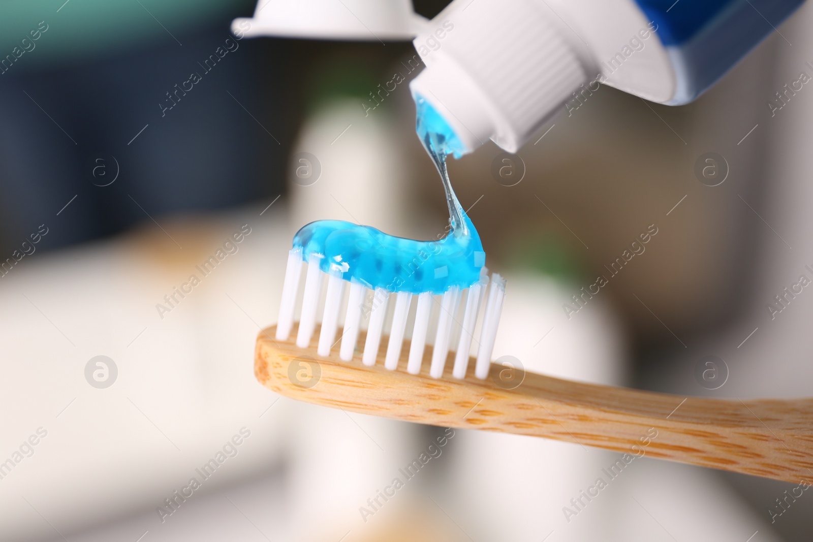 Photo of Applying toothpaste on brush against blurred background, closeup