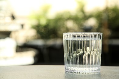 Photo of Glass of fresh water on light grey table outdoors, closeup. Space for text