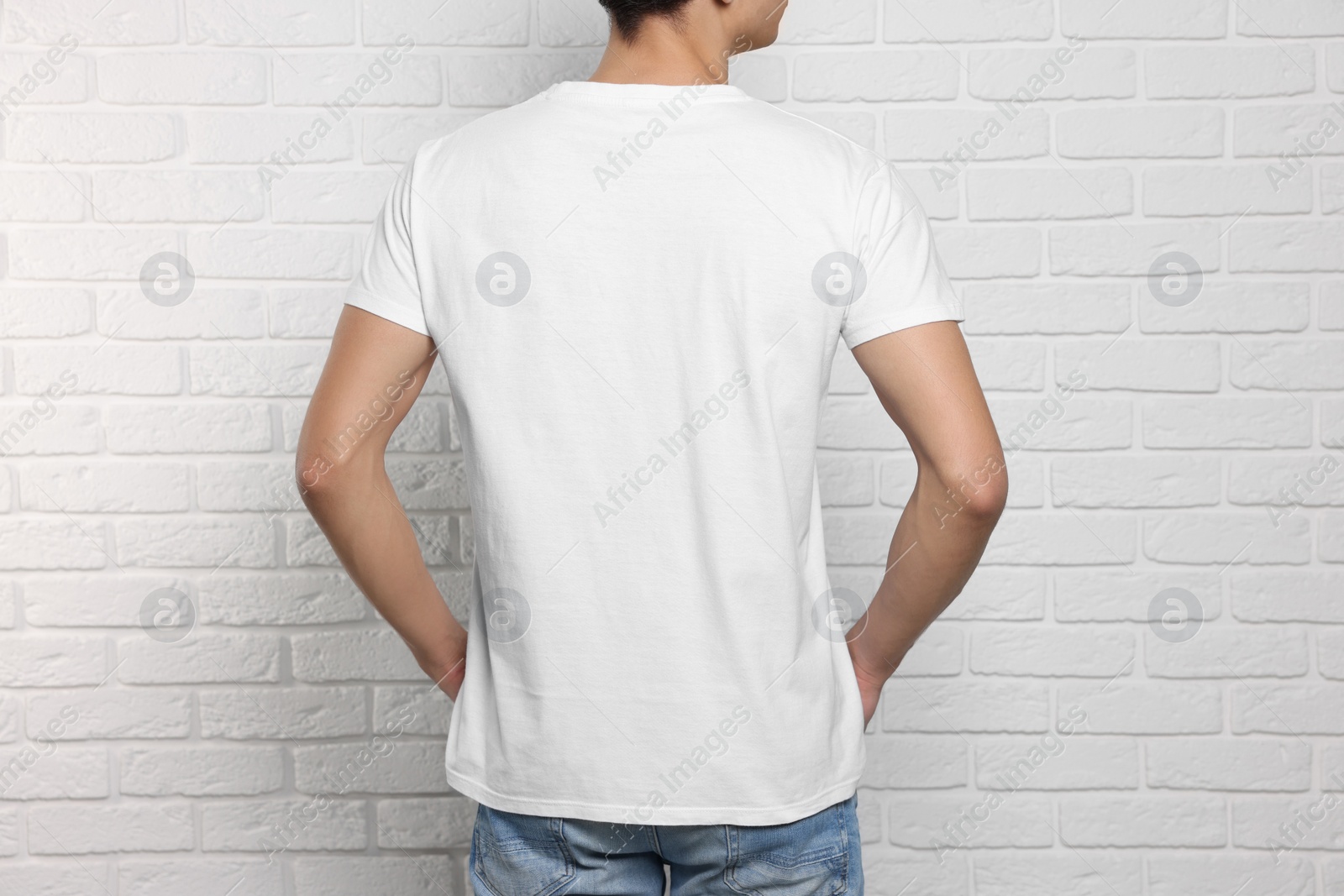 Photo of Man wearing stylish t-shirt near white brick wall, back view. Mockup for design