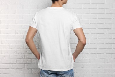 Photo of Man wearing stylish t-shirt near white brick wall, back view. Mockup for design