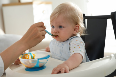 Mother feeding her cute little baby with healthy food at home