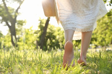 Photo of Woman with straw hat walking barefoot on green grass outdoors, closeup. Space for text