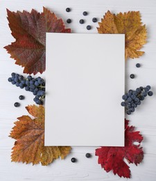 Photo of Flat lay composition with blank card, autumn leaves and grapes on white wooden table. Space for text