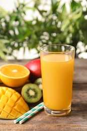 Photo of Tasty tropical drink with mango and fresh fruits on wooden table against blurred background