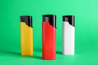 Stylish small pocket lighters on green background