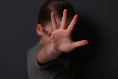 Photo of Child abuse. Girl making stop gesture near grey wall, selective focus