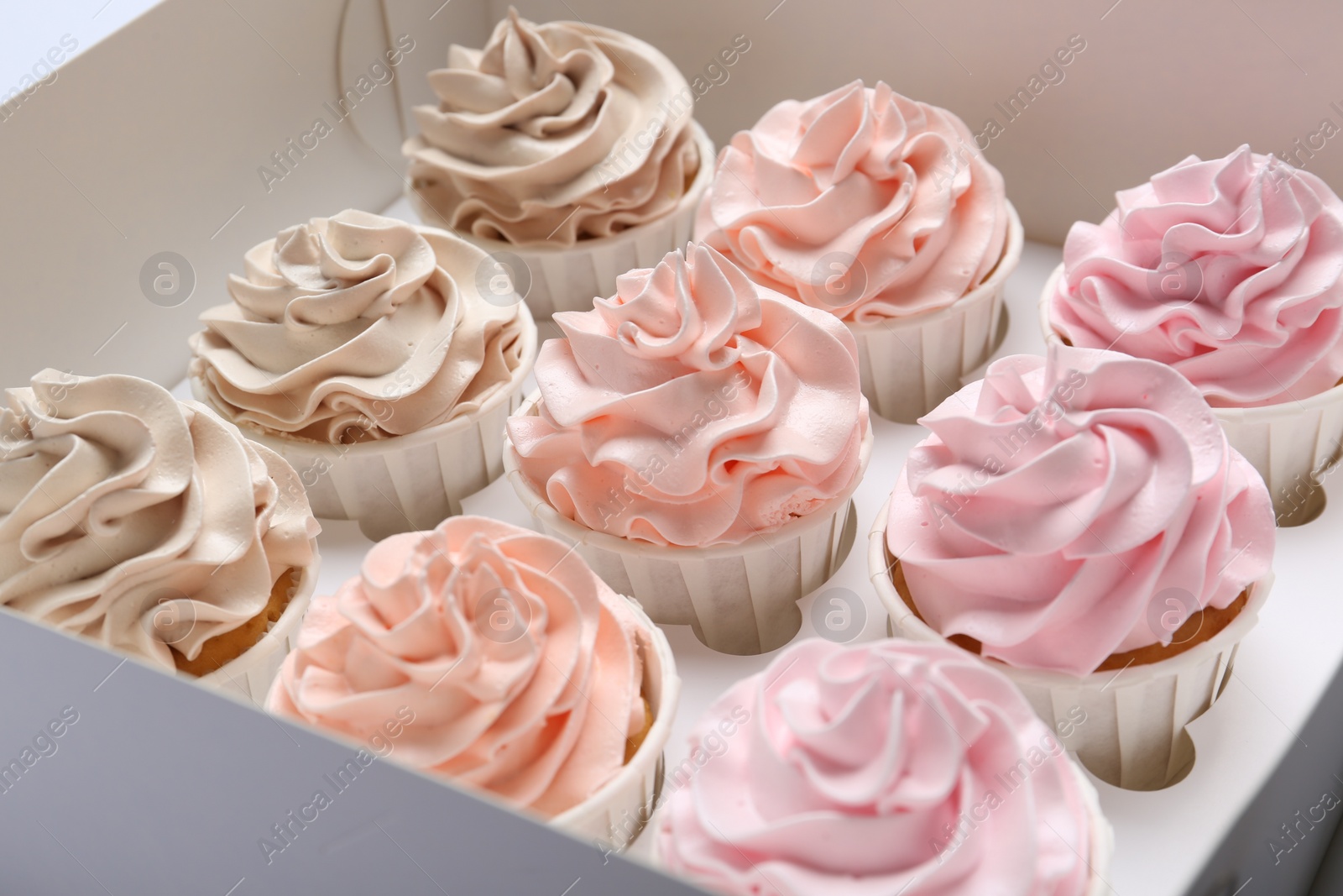 Photo of Many tasty cupcakes with colorful cream in box, closeup