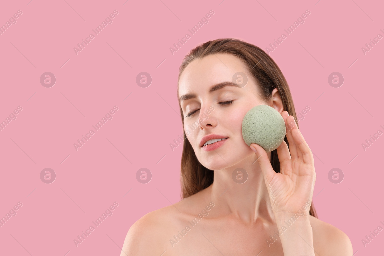 Photo of Young woman washing her face with sponge on pink background. Space for text