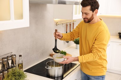 Man pouring delicious soup into bowl in kitchen