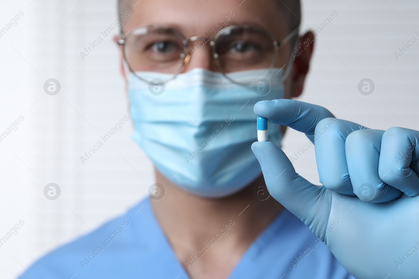 Photo of Doctor holding pill on light background, selective focus. Space for text