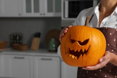 Photo of Woman holding carved pumpkin for Halloween in kitchen, closeup. Space for text