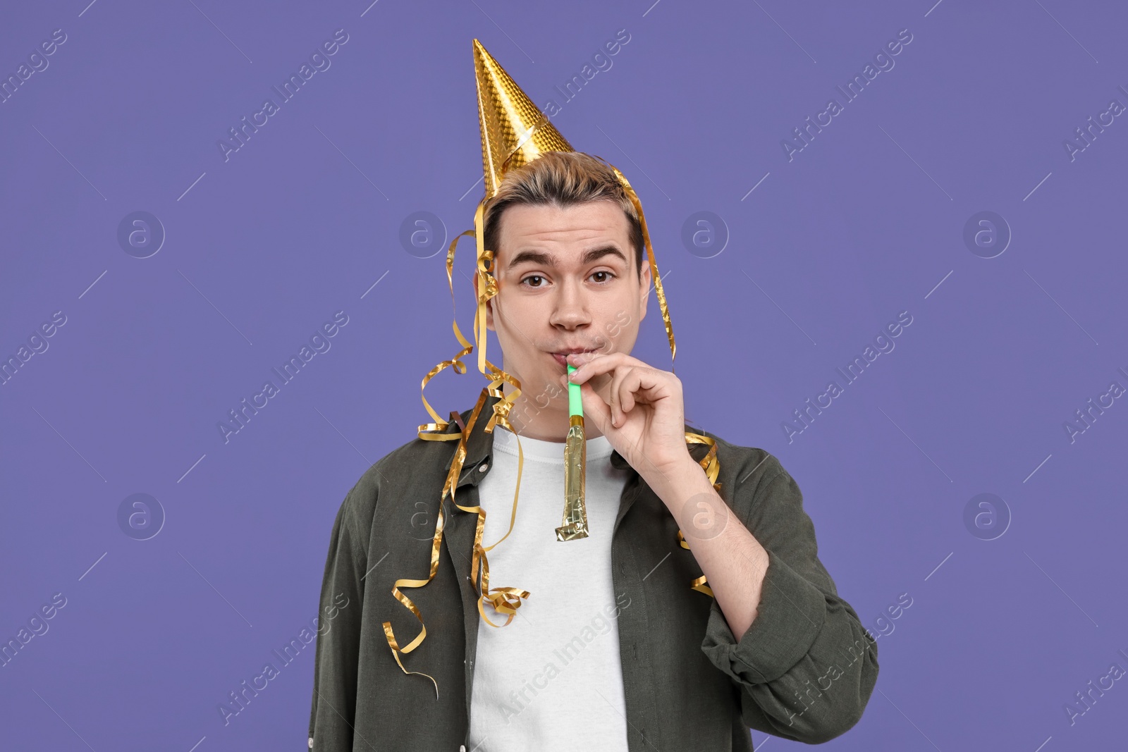 Photo of Young man with party hat and blower on purple background