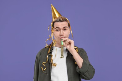 Young man with party hat and blower on purple background