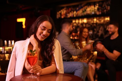 Friends spending time together in bar. Beautiful woman with fresh alcoholic cocktail at table, space for text