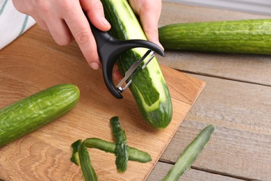 Photo of Woman peeling cucumber at wooden table, closeup