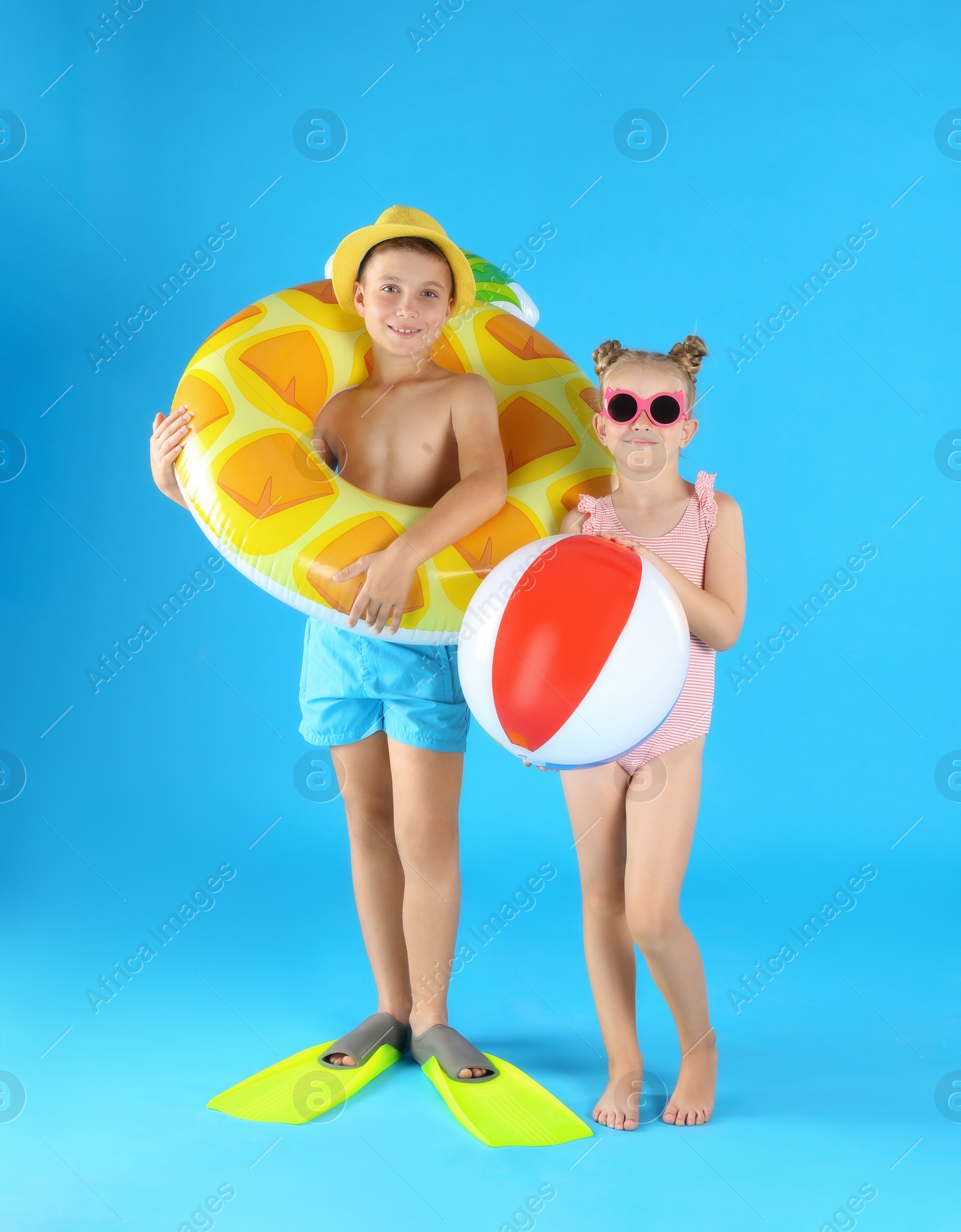 Photo of Cute little children in beachwear with inflatable toys on light blue background