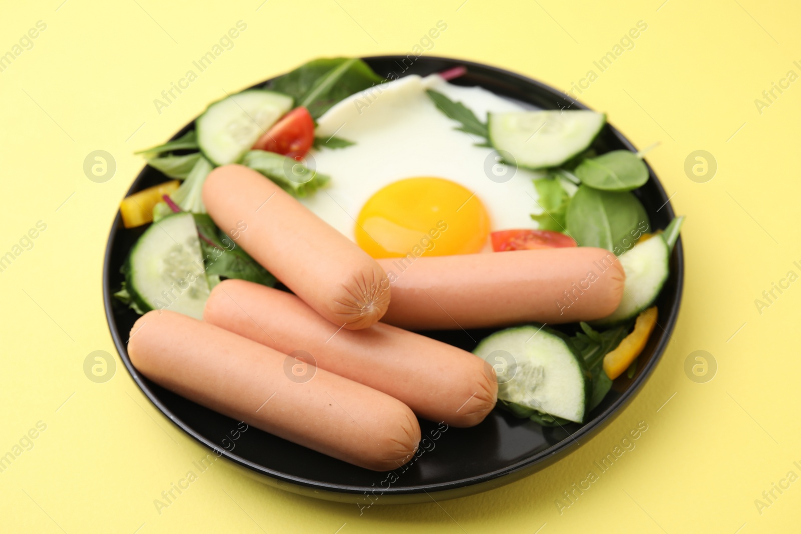 Photo of Delicious breakfast with boiled sausages and fried egg on yellow background