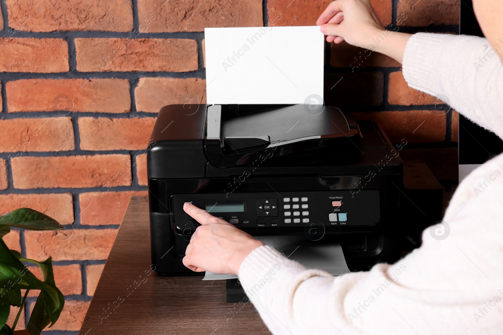 Photo of Woman using modern printer at wooden desk in home, closeup