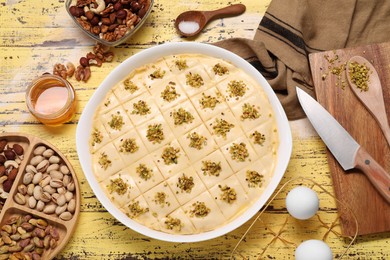 Photo of Making delicious baklava. Raw dough with ingredients on yellow wooden table, flat lay