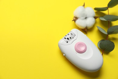 Photo of Modern epilator, eucalyptus branch and fluffy cotton flower on yellow background, above view. Space for text