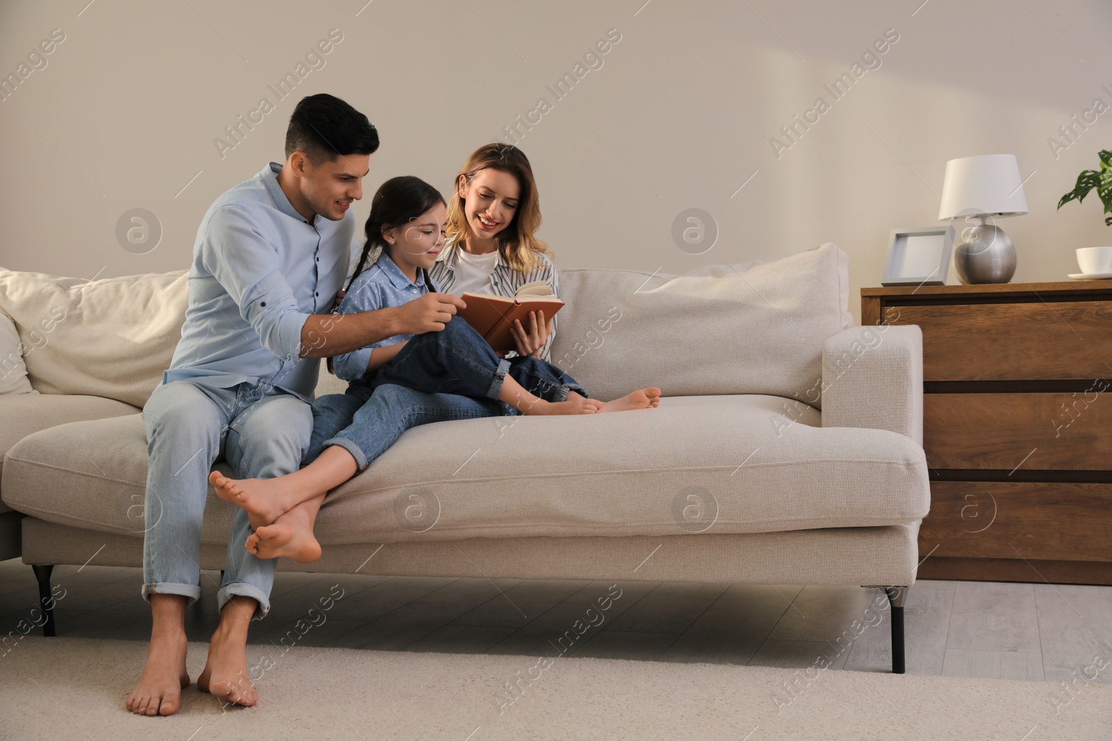 Photo of Family with little daughter reading book on sofa in living room