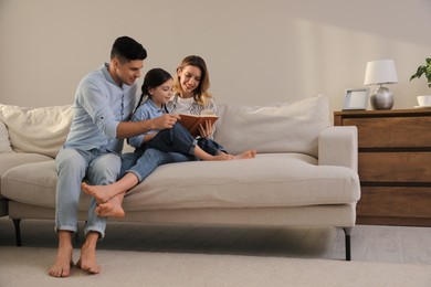 Photo of Family with little daughter reading book on sofa in living room