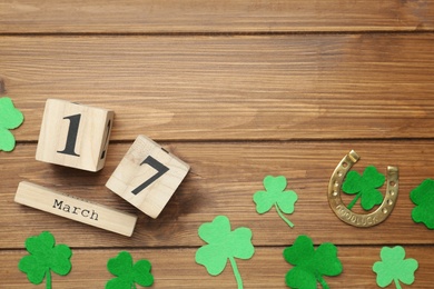 Decorative clover leaves, horseshoe and block calendar on wooden background, flat lay with space for text. St. Patrick's Day celebration