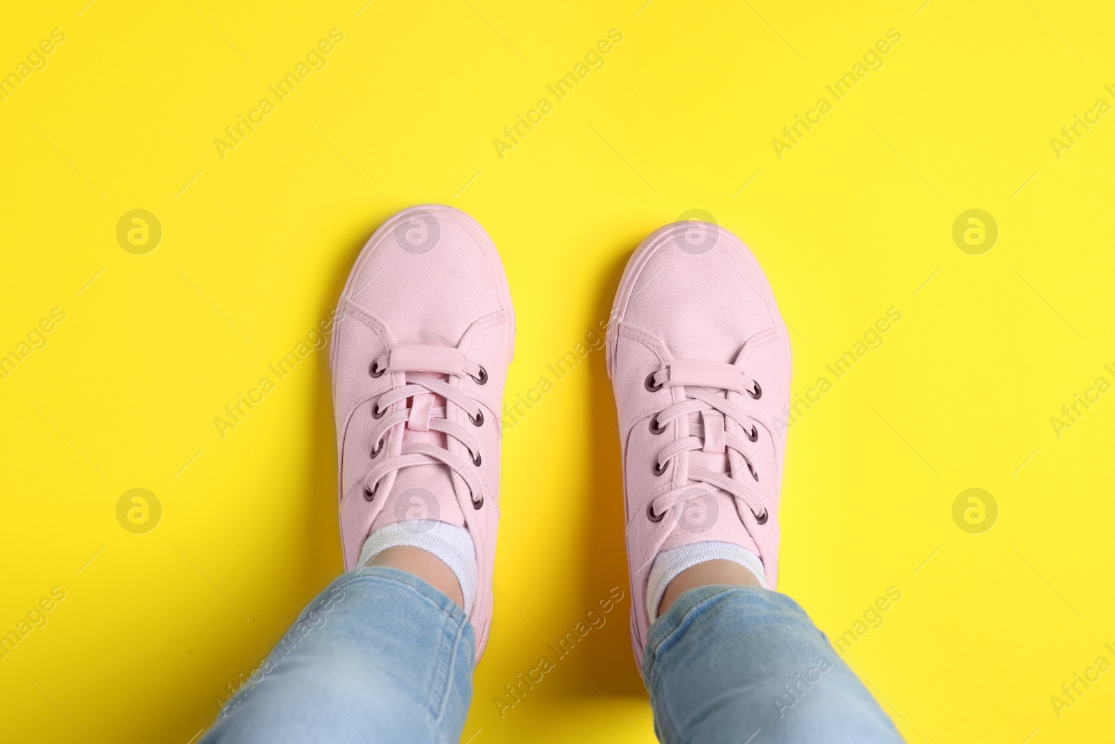 Photo of Woman in stylish sneakers standing on yellow background, top view