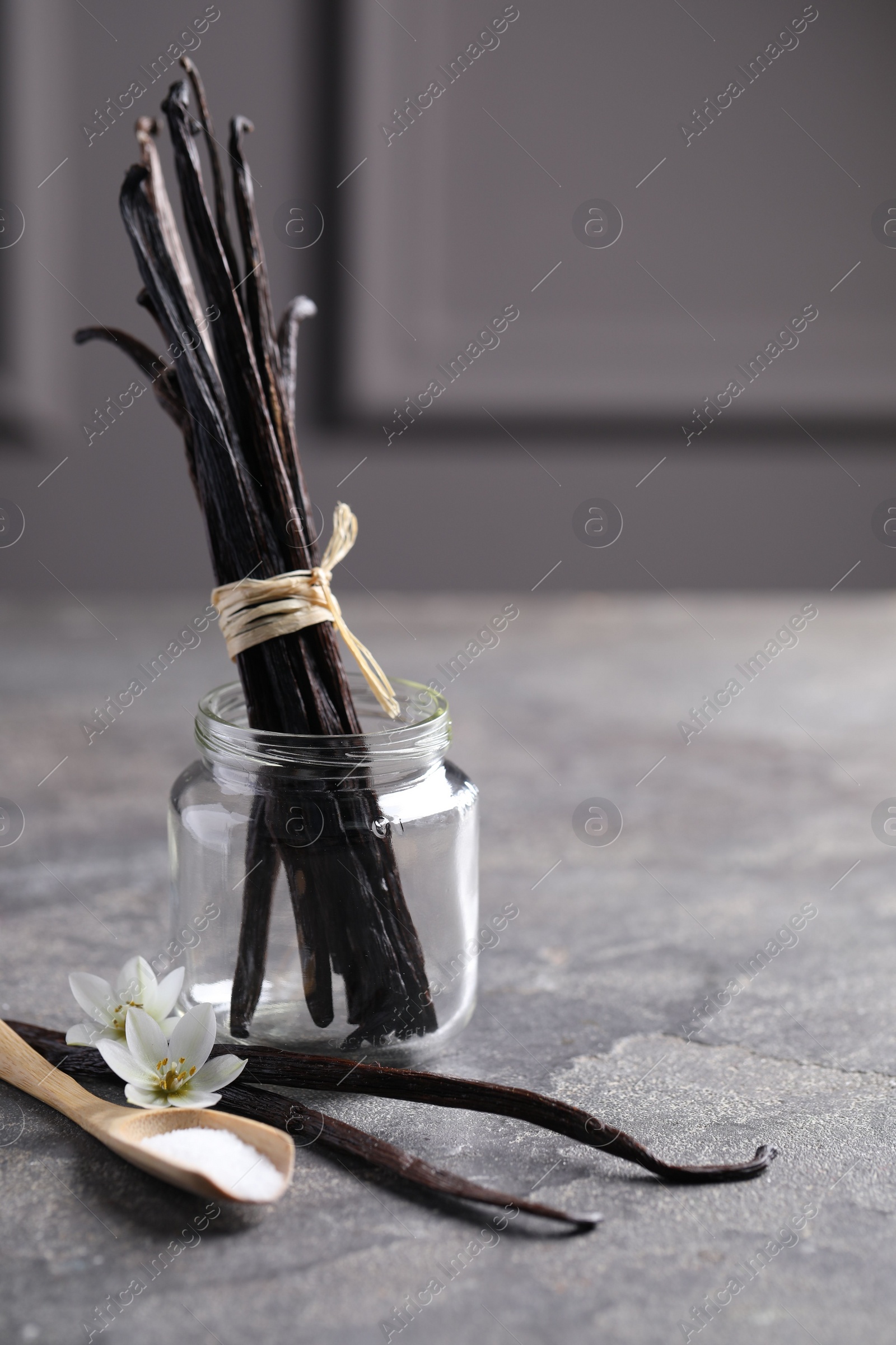 Photo of Spoon with sugar, flowers and vanilla pods on grey textured table. Space for text