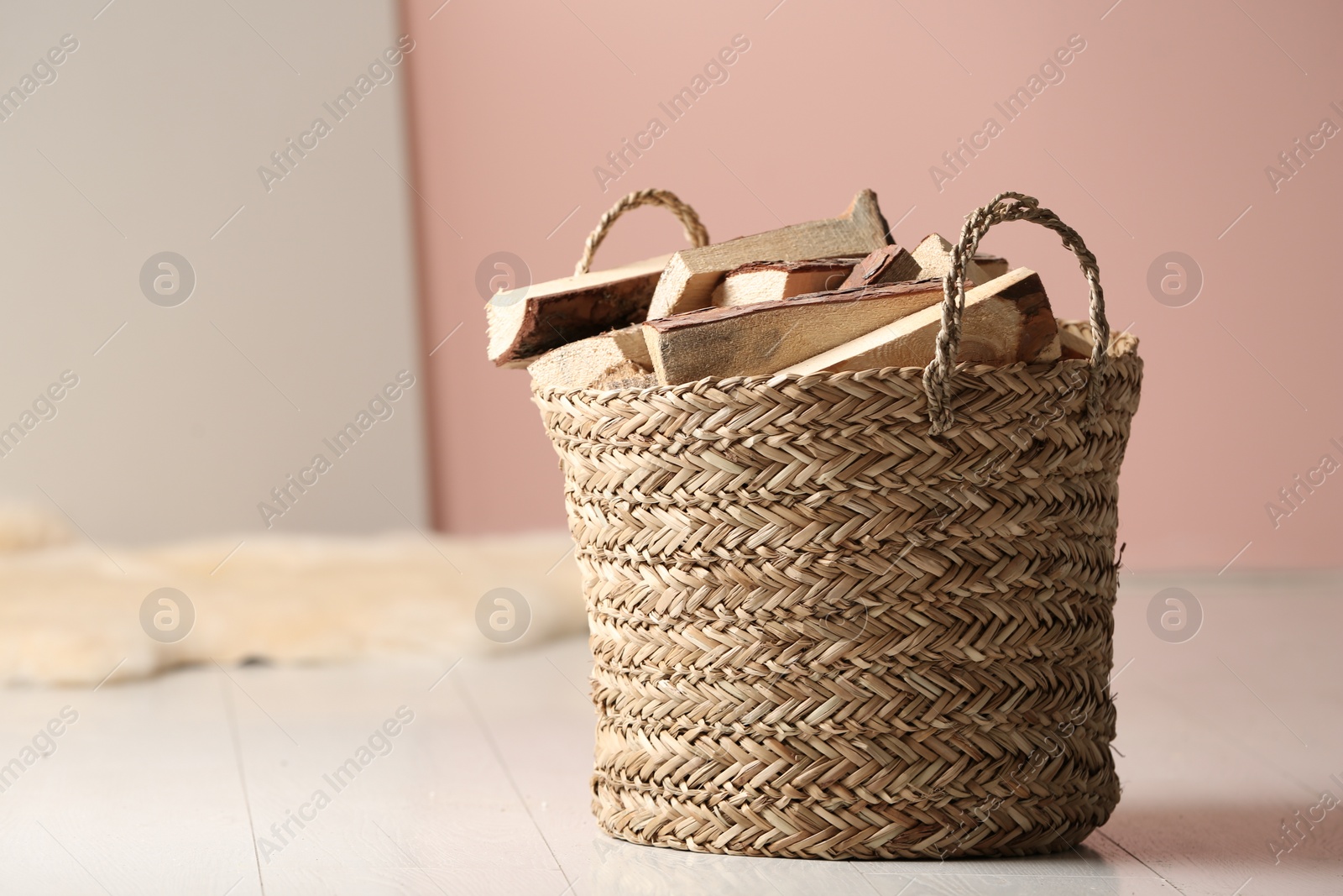 Photo of Wicker basket with cut firewood on white floor indoors