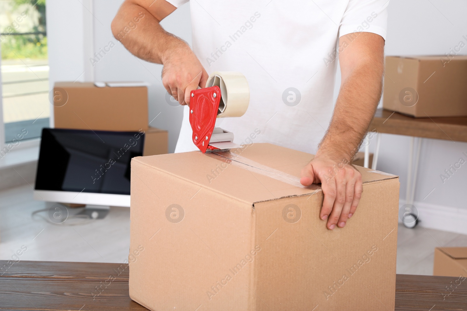 Photo of Young worker packing cardboard box in room, closeup. Moving service