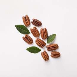 Delicious pecan nuts and green leaves on white background, flat lay